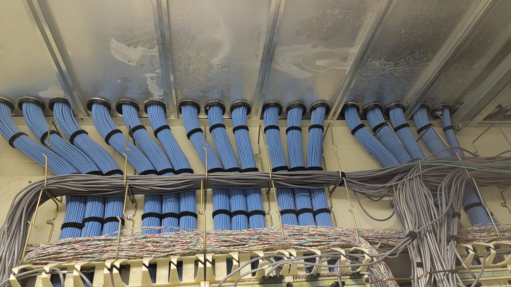 Bundles of blue and grey network cable entering a network room through wall sleeves