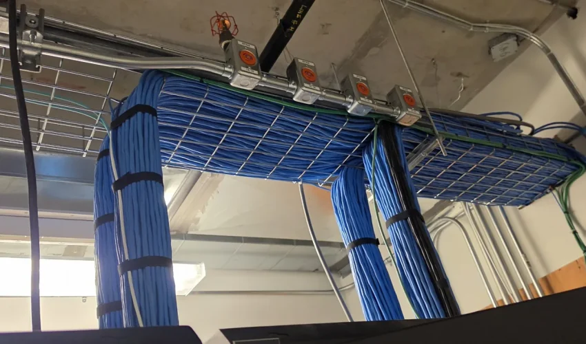 Bundles of blue horizontal cables in wire basket tray dropping into network racks in a telecom room