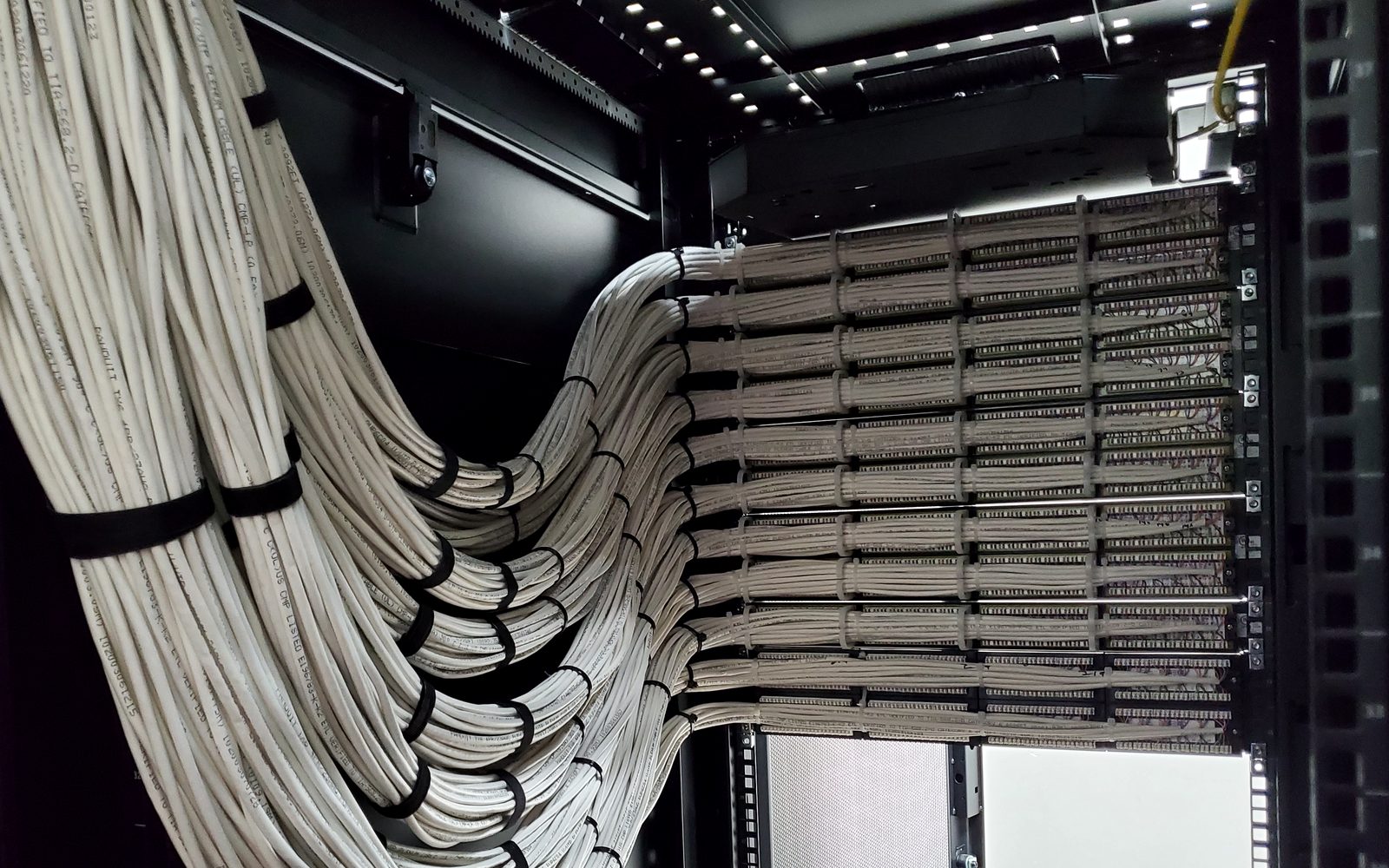 White Cat6 cable looms sweeping into rows of patch panels inside a network cabinet
