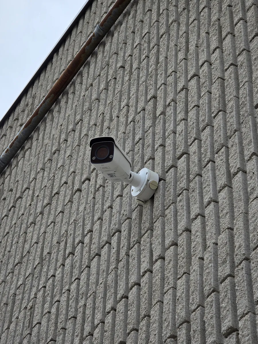 Bullet camera with a varifocal lens mounted high on a concrete block warehouse wall