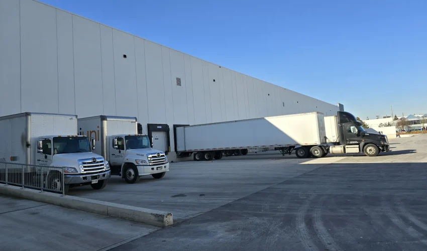 Box trucks and a tractor-trailer backed into dock doors along a large warehouse wall